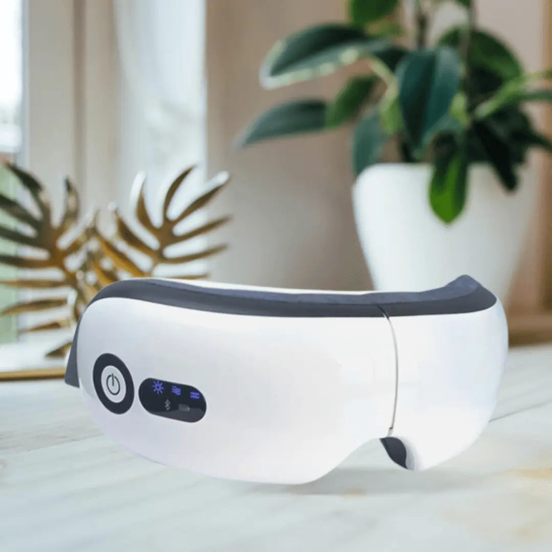 White Dreemo Elixir One™ Eye Massager on a wooden table near a plant, offering heat, vibration, and air pressure for daily eye relaxation and comfort.